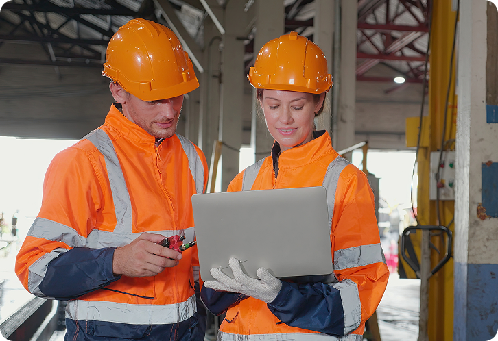 Two construction workers look at laptop onsite.